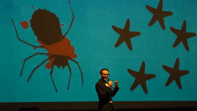 On stage with a mic before a slide of a squashed spider among starfish