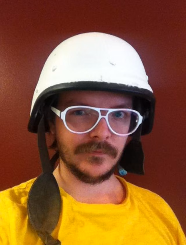 A composite helmet painted white, white aviator glasses and a yellow tee