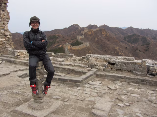 Arms crossed on a stone post, the Great Wall behind