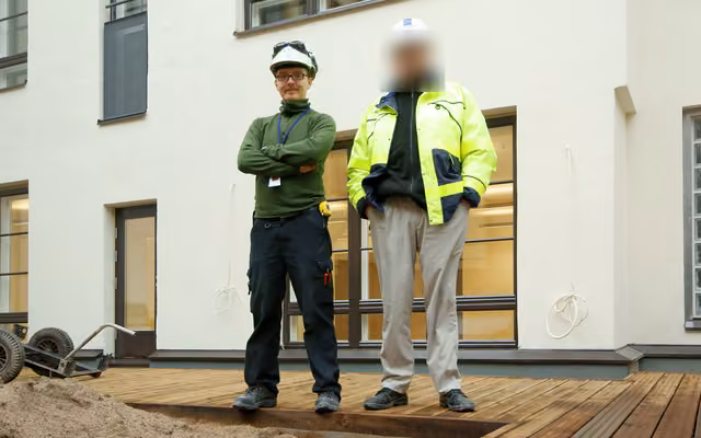 On a building site in a white helmet, beside a colleague whose face is blurred