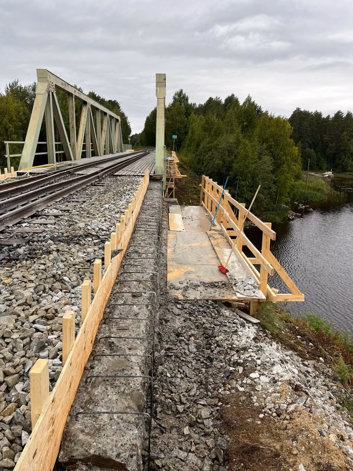 A steel truss railway bridge over a river, timber formwork along the track