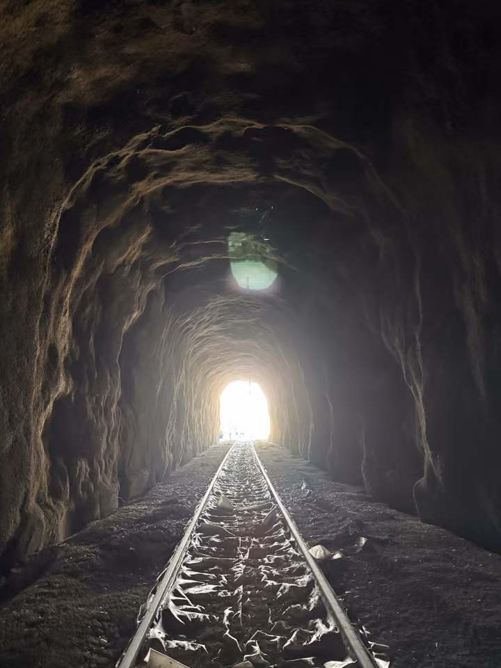 A railway tunnel in bare rock, daylight at the far end